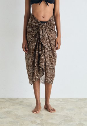 Wickelrock mit Leopardenmuster aus leichtem Stoff, vorne geknotet, mit fließender Form und transparenter Textur, der oberhalb der Knöchel getragen wird.