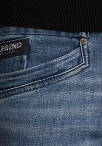 Svijetloplavi traperice s klasičnim krojem; vidljivo šivanje, lagano izblijeli izgled i brendirana oznaka "LEGEND." Prikazan detalj prednjeg džepa.