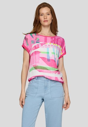 Kurzärmliges, pinkes Shirt mit mehrfarbigen, abstrakten Mustern. Weicher Stoff, lockere Passform und runder Halsausschnitt, kombiniert mit hellblauen Jeans.