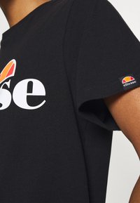 Camiseta de algodón negra con un logo blanco de "ellesse" en el pecho, mangas cortas y un pequeño logo en la manga.