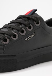 Musta nahkakengät, joissa on teksturoitu pinta, pyöreät silmukat ja mustat nauhat. Varusteena metallinen "TOMMY"-logo ja värikäs raidallinen yksityiskohta kantapäässä.