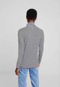 Randig turtleneck i svart och vitt med långa ärmar, tillverkad av ett lätt material. Baksidan visar en figurnära form och hög halsdesign.