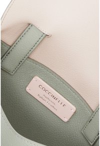 Intérieur d'un sac à main en cuir vert et rose avec une étiquette indiquant "COCCINELLE Cuir Italien Authentique." Texture lisse, design simple.