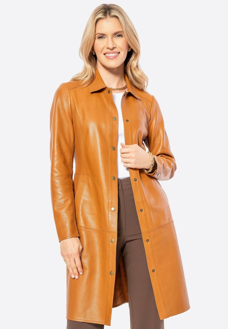 Tan lederen lange jas met een kraag, drukknoopsluiting, zijzakken en een gladde afwerking, gedragen over een wit topje en bruine broek.