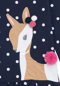 Marineblaues Kleid mit weißen Punkten, das ein besticktes Reh-Design, Pompons in Pink, Weiß und Marineblau sowie einen strukturierten Rüschensaum aufweist.