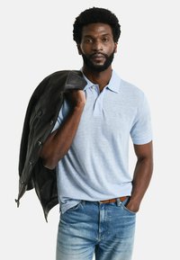 Ljusblå pikétröja med korta ärmar och lös passform, i kombination med denimjeans och en svart läderjacka slängd över axeln.