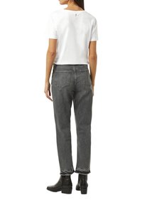 Weißes Baumwoll-T-Shirt mit Knopfdetails am Rücken, kombiniert mit grauen, hochgeschnittenen geraden Jeans mit fransigem Saum und zwei Gesäßtaschen.