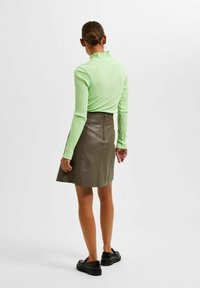 Maglione a collo alto a coste verde chiaro, aderente. Abbinato a una gonna in pelle oliva di lunghezza al ginocchio con zip sul retro. Scarpe nere senza lacci.