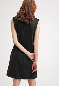 Robe noire sans manches à coupe droite, avec une texture lisse et un détail de couture subtile à l'arrière. Design simple et minimaliste.
