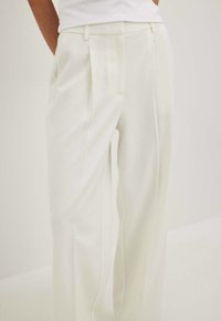 White pleated trousers with side pockets, a relaxed fit, and smooth texture. The waistband features belt loops for adjustable styling.