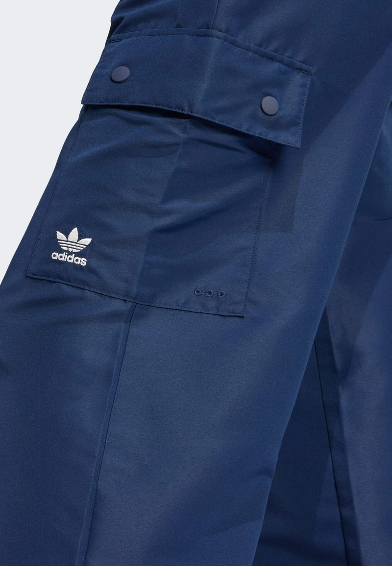 Navy blue cargo pants with a smooth texture, featuring a flap pocket, button accents, and the white Adidas logo.