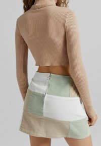 Beige žebrovaný rolák zkrácený top spárovaný s mini sukní z vícebarevného patchworku, která má zelené, béžové a bílé části a zadní zip.