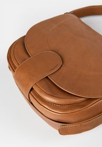 Brun læderhåndtaske med en buet klap, syede detaljer og en bred rem. Flad design med en glat, tekstureret overflade.