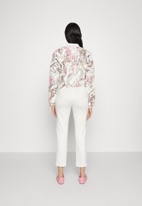 Giacca con motivo floreale in bianco, rosa e beige; abbinata a pantaloni bianchi a gamba affusolata e pantofole di un rosa chiaro.