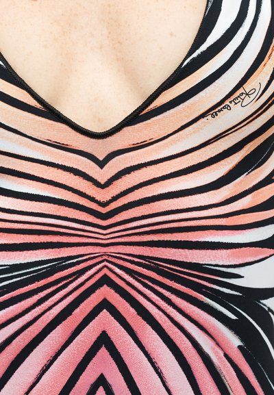 Gros plan sur la poitrine d'une femme vêtue d'un vêtement à col en V avec un motif rayé rose, noir et blanc formant un dessin symétrique.