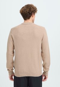 Beige Strickpullover mit Rundhalsausschnitt, gerippten Bündchen und Saum. Der Stoff wirkt weich mit einer dezenten Textur und minimalen Details.