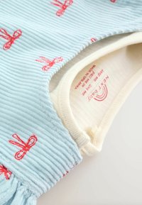 Ljusblå ribbad babytopp med röd rosettbroderi, med en krämfärgad halsringning och mjukt material. Skötselguide synlig inuti.