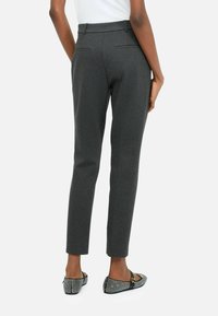 Pantaloni grigi scuri su misura con una texture liscia, vestibilità slim e tasche posteriori, abbinati a mocassini a righe bianchi e neri.