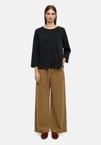 Czarny bawełniany sweter z okrągłym dekoltem i opuszczonymi ramionami, zestawiony z szerokimi brązowymi spodniami. Miękka tekstura, minimalistyczny design i luźny krój.
