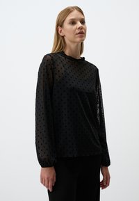 Schwarze Bluse aus transparenter Stoff mit Punktmuster, langen Ärmeln mit elastischen Bündchen und lässigem Schnitt.