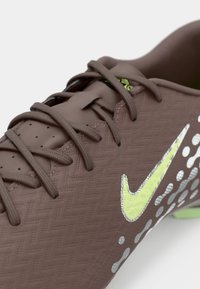 Καφέ ποδοσφαιρικό παπούτσι με υφασμάτινη επιφάνεια, που διαθέτει πράσινο λογότυπο Nike, γκρι σχέδιο με κουκκίδες και καφέ κορδόνια. Κοντινή λήψη στο τμήμα των δαχτύλων.