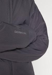 Čierna zateplená bunda z textúrovaného materiálu. Obsahuje predný zips a logo "DIDRIKSONS" na ľavom rukáve.