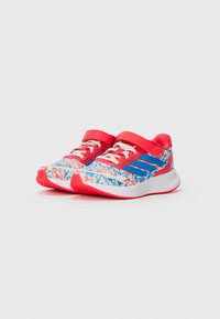 Chaussures de sport pour enfants avec des motifs abstraits rouges, bleus et blancs, des lacets blancs, des sangles rouges et des semelles blanches rembourrées.