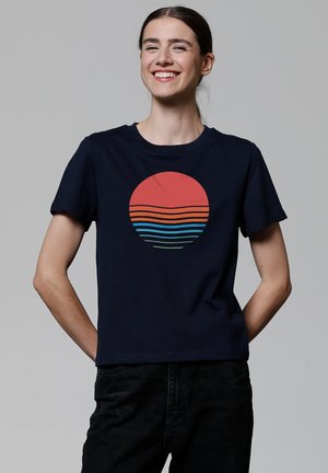 T-shirt en coton bleu marine avec un graphique circulaire représentant un soleil rouge et des lignes horizontales multicolores en bleu, orange et vert. Manches courtes.