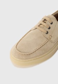 Šviesiai rudos veliūrinės bateliai su raišteliais, apvaliu pirštu, kontrastinga siuvinėjimu ir šviesos spalvos guminėmis padais. Sklandi tekstūra su minimaliais akcentais.