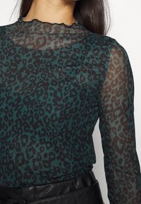 Transparent blåblus med svart leopardtryck, med en scallop-nacke och långa ärmar. Lätt tyg med en slät yta.