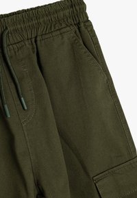 Olivgrön cargo-byxor med elastisk midja och dragsko. Har sidofickor och en texturerad tyg med synliga sömmar.