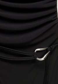 Tissu noir avec une texture plissée, mettant en valeur un accent en D en argent et des cordons noirs noués, soulignant un design ajusté.