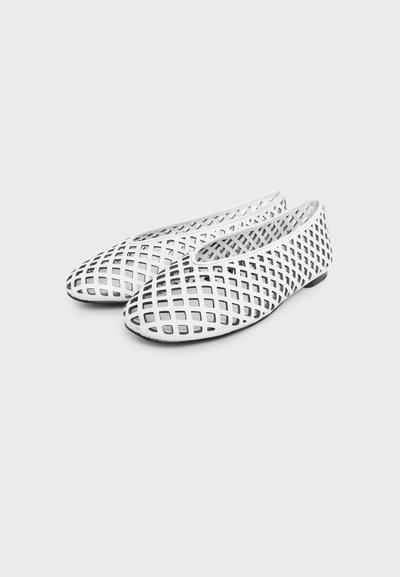 Chaussures plates blanches avec un design ajouré en forme de treillis, bout arrondi et semelle noire, affichées sur un fond clair et neutre.