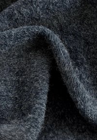 Weiche, strukturierte Wollstoff in Dunkelgrau, mit einer flauschigen, gewebten Oberfläche und losen Fasern. Das Material ist üppig und fällt leicht.