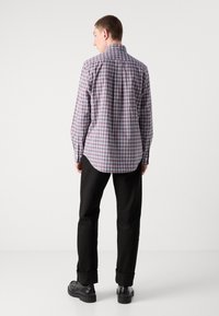 Camicia a quadri con colletto a punte, caratterizzata da motivi blu, rossi e bianchi. Abbinata a pantaloni e scarpe nere.