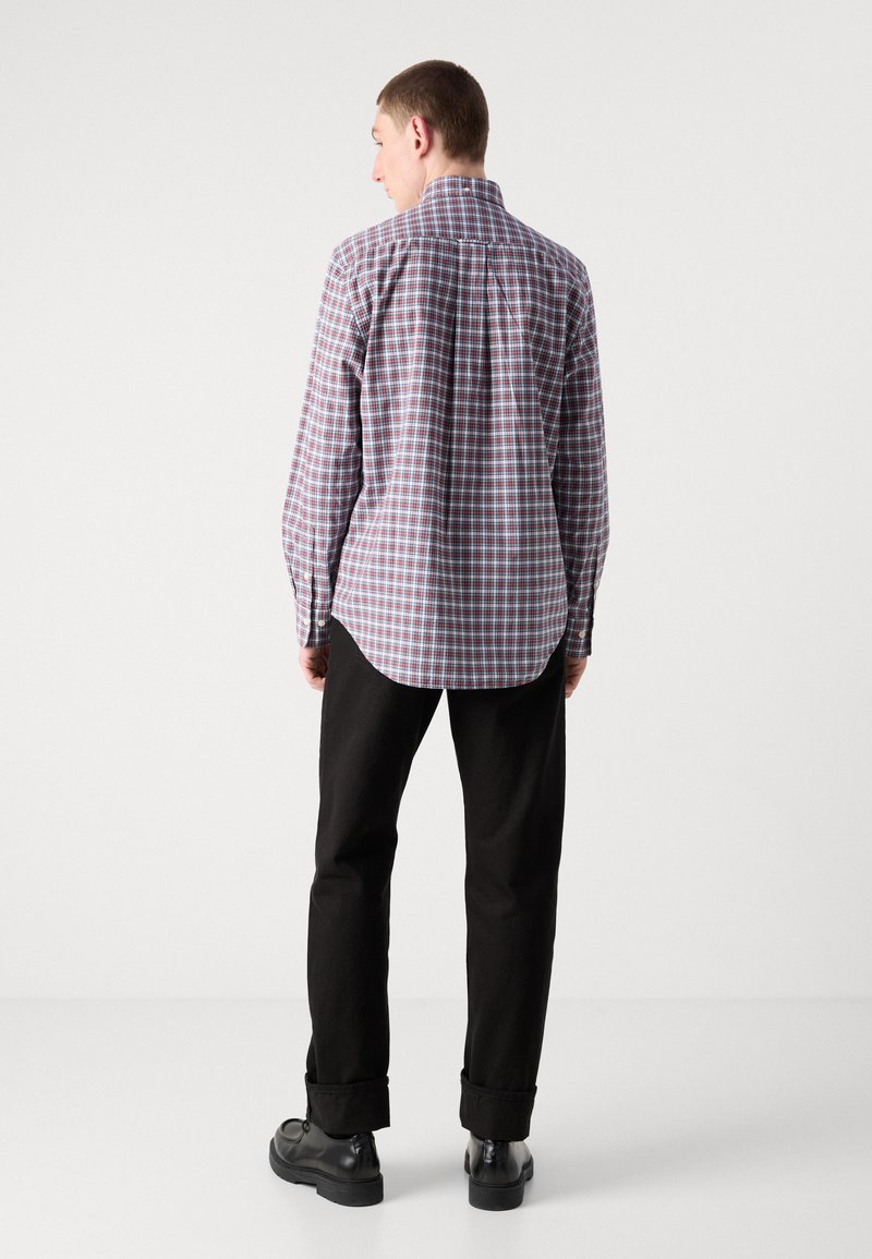 Karierte Button-up-Bluse mit Kentkragen, mit blau, rot und weißen Mustern. Kombiniert mit schwarzen Hosen und Schuhen.