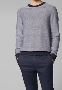 Stickad crewneck-tröja i blått med ett texturerat mönster, med ribbade ärmslut och nederkant. Matchad med mörkblå byxor.