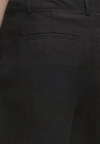 Κοντινή λήψη μαύρου υφασμάτινου παντελονιού που δείχνει μια πίσω τσέπη με διακριτική υφή ψαροκόκαλου και θηλιά ζώνης στη μέση.