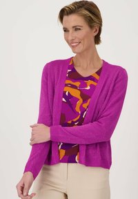 Fuchsia brei cardigan met glinsterende textuur, open voorkant, geribbelde manchetten en zoom. Gecombineerd met een gemêleerd multicolor top en neutrale broek.