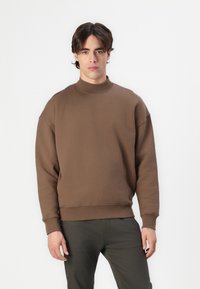 Brown pullover sweatshirt with a high collar, dropped shoulders, ribbed cuffs, and hem. Made of soft fabric with a smooth texture.