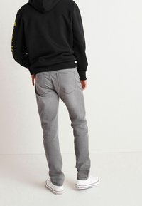 Jeans de mezclilla gris con corte slim, que presentan bolsillos traseros, una altura media y detalles de costura sutiles. Combinados con una sudadera negra y zapatillas blancas.
