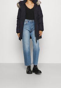 Marinblå parkas med huva med konstpäls, i kombination med ljusblå vida jeans och svarta kraftiga stövlar, med en avslappnad och ledig passform.