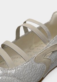 Ballerine plate grise avec texture en cuir craquelé, dotée de trois brides élastiques et du logo de la marque, intérieur avec motif répétitif de texte beige clair.