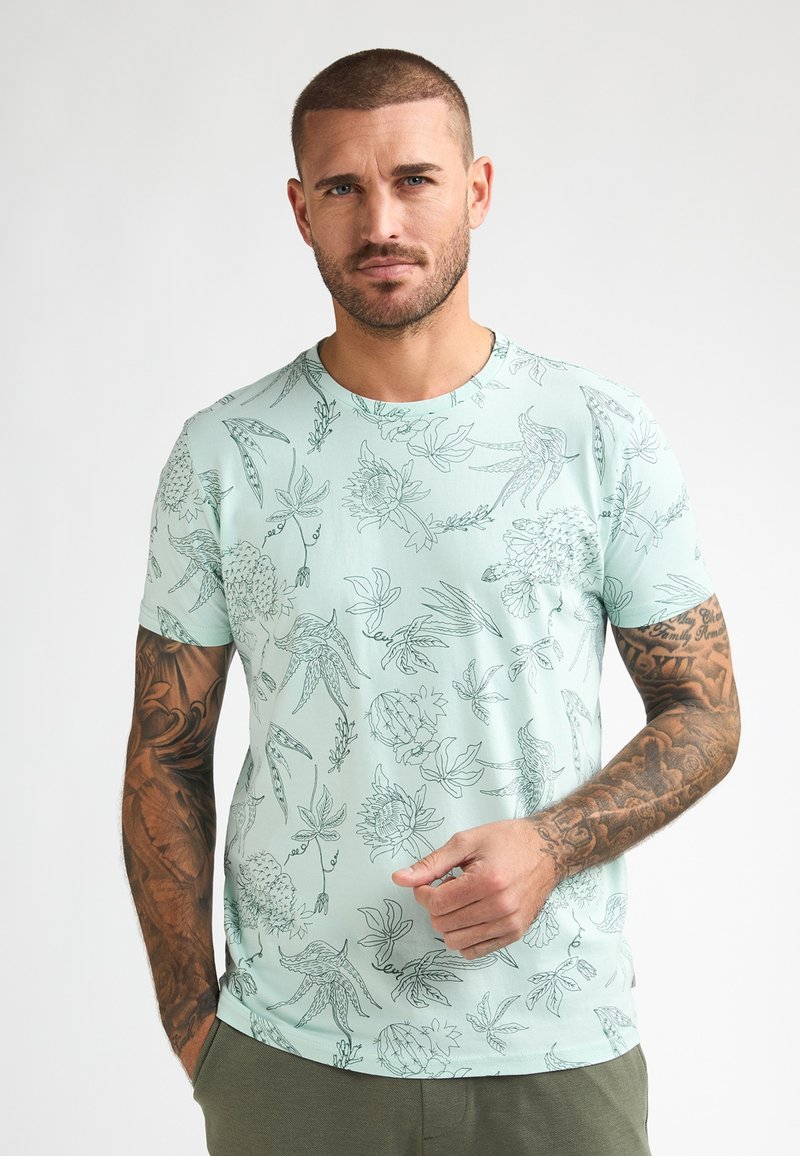 Licht muntgroen T-shirt met korte mouwen en een botanisch lijntekeningpatroon. Ronde hals, zachte stof, reguliere pasvorm en subtiele textuur.