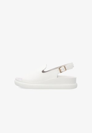 Witte open teen slingback sandaal met een dikke zool en een gouden gesp op de verstelbare band, zijaanzicht.