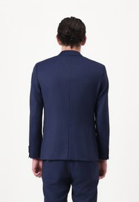 Blazer navy ajustado con una textura suave, hombros estructurados, abertura simple y pantalones a juego, con detalles de botones en las mangas.