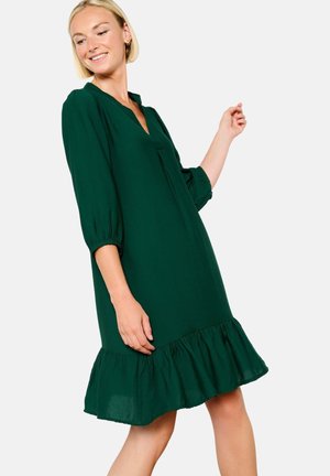 Green, knee-length dress made of lightweight fabric. Features a V-neck, 3/4 sleeves, and a ruffled hem. Simple and relaxed fit design.