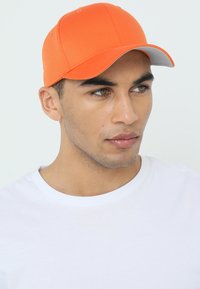 Cappellino da baseball arancione con visiera grigia, realizzato in tessuto e con cuciture a vista. Indossato da una persona con un'espressione neutra.