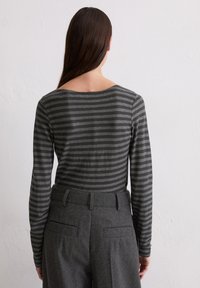Sivý dlhý rukáv s tmavosivými pruhmi a širokým výstrihom. V kombinácii s elegantnými sivými nohavicami s zadnými vreckami.