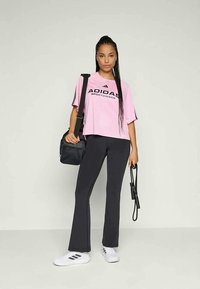 Rosa T-skjorte med kort erme fra Adidas med svart logo, kombinert med svart flagrende bukser og hvite joggesko med tre svarte striper.